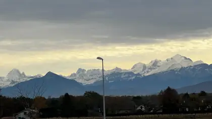 Snow-covered Alps behind a lamp post and fields on a cloudy day