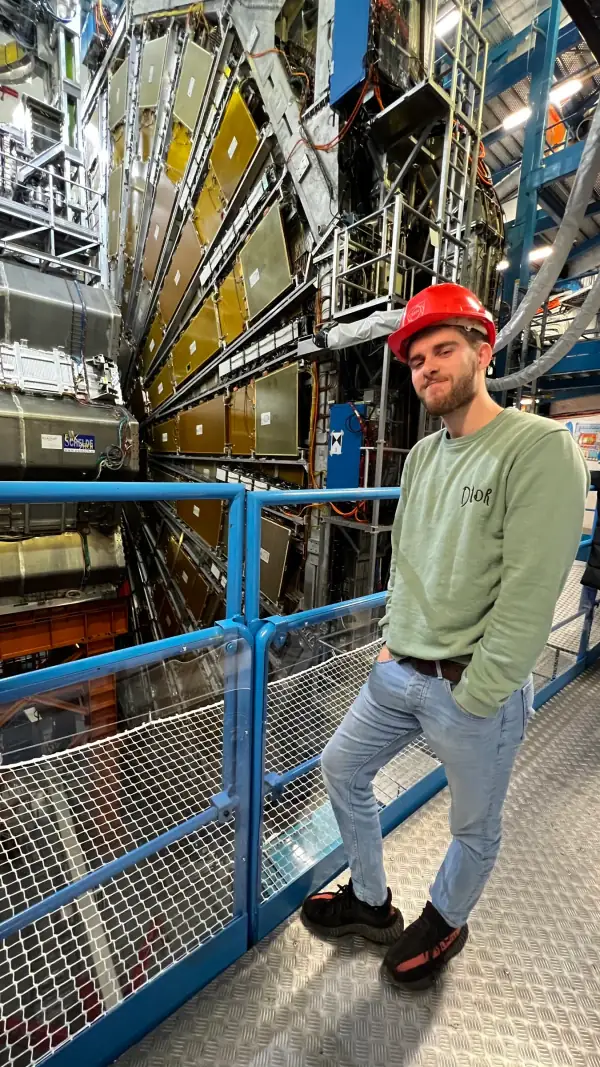 Me in a red hard hat on a walkway next to a huge particle detector at CERN