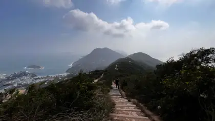 A hiker on a stone path along a ridge above the sea