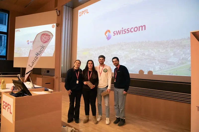 Four people on stage in front of the Swisscom slide at EPFL, two holding small prizes